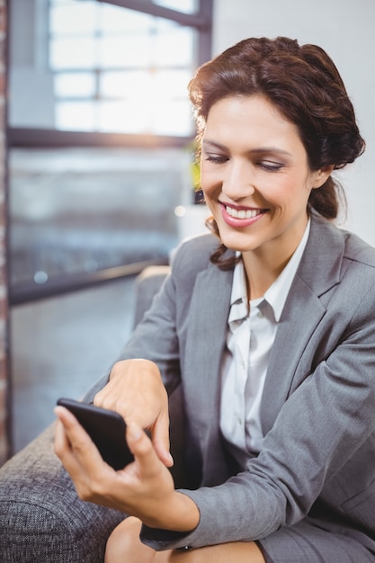 Zdjęcie bizneswoman ono uśmiecha się podczas gdy patrzejący telefon komórkowego