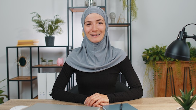 Bizneswoman pracująca uśmiechając się przyjaźnie do kamery i gesting hello assalamu alaikum w biurze domowym