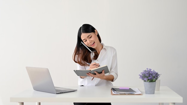 Bizneswoman robi notatki podczas rozmowy telefonicznej z kimś przy biurku