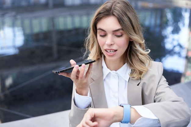 Bizneswoman sprawdza czas na cyfrowym zegarku i nagrywa wiadomość głosową, aranżuje spotkanie na zewnątrz