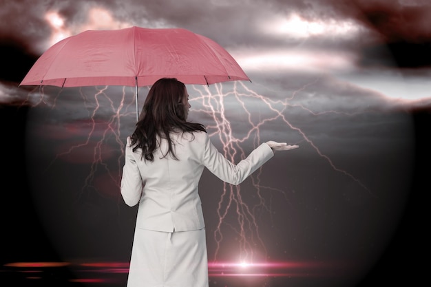 Bizneswoman trzyma parasol przeciw burzliwemu ciemnemu niebu z błyskawicami