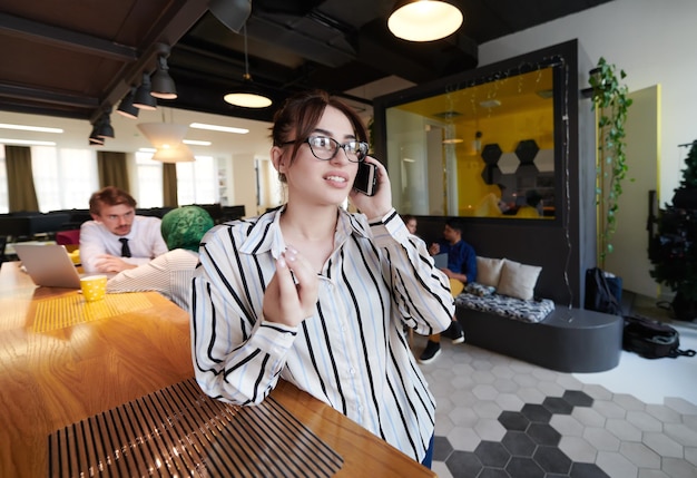 bizneswoman w okularach korzystający z telefonu komórkowego w nowoczesnym wnętrzu biurowym na otwartym planie