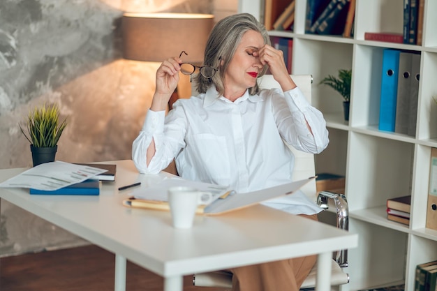 Bizneswoman w średnim wieku w białej bluzce wygląda na zmęczoną po pracy