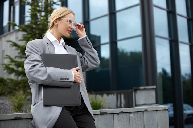 Bizneswoman w stylowych okularach trzymająca laptopa patrząca na ulicę