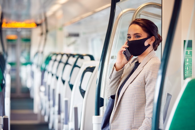 Bizneswoman w wagonie pociągu rozmawia przez telefon komórkowy nosząc maski na twarz podczas pandemii