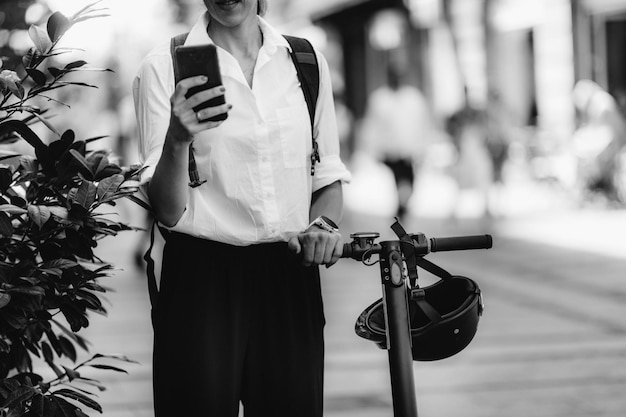Bizneswoman z inteligentnym telefonem i skuterem elektrycznym w mieście