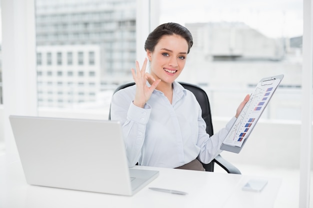 Bizneswoman z wykresami i laptopem gestykuluje ok podpisuje wewnątrz biuro