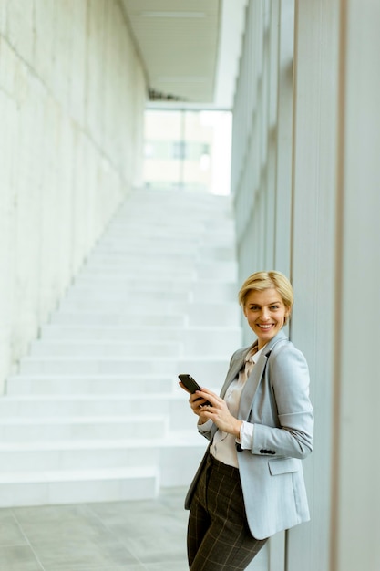 Bizneswoman za pomocą telefonu komórkowego na nowoczesnym korytarzu biurowym