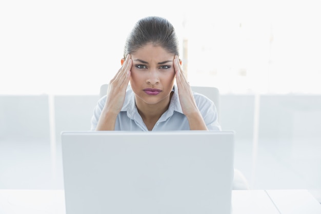 Bizneswomanu cierpienie od migreny z laptopem przy biurem