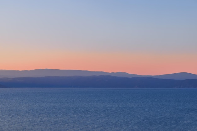 Błękitna godzina zmierzchu nabiera głównie niebieskiego odcienia na wzgórzach nad wodą morską, różowa poświata horyzontu