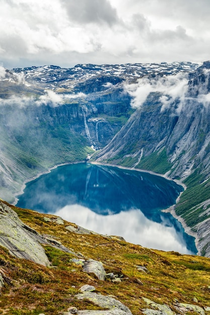 Błękitne jezioro otoczone stromymi klifami ukrywającymi się w chmurach Hrabstwo Odda Hordaland Norwegia