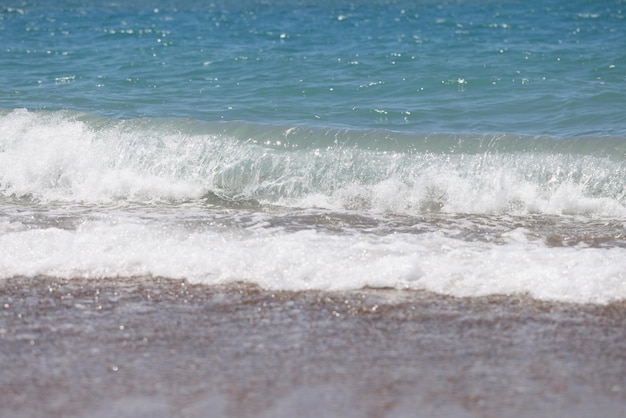 Błękitne morskie fale z białą pianką na morskiej piaszczystej plaży