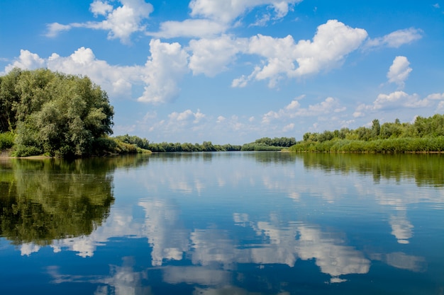 Błękitne piękne niebo z rzeką. Chmury są wyświetlane w spokojnej wodzie. Na horyzoncie zielony brzeg Dniestru, miejsce do wędkowania