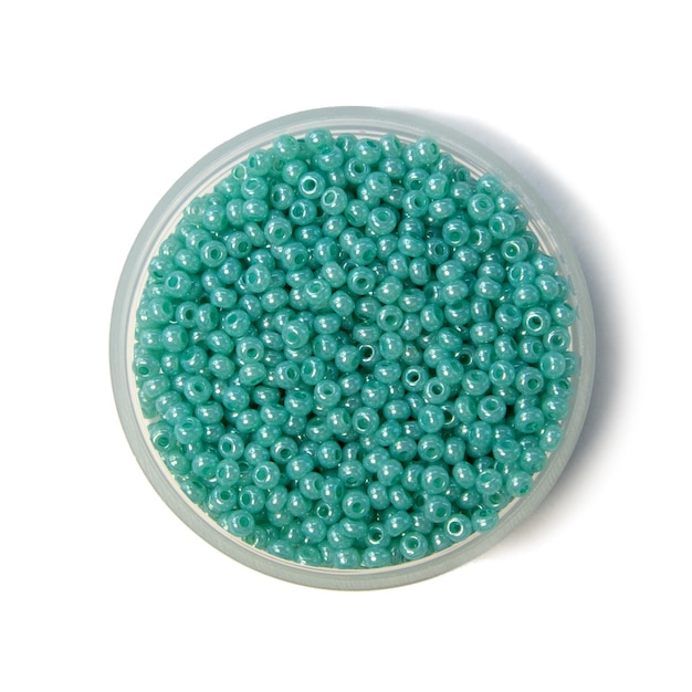 Zdjęcie błękitni koraliki do robótek ręcznych perłowy kolor w plastikowym słoju na białej sosnowej desce
