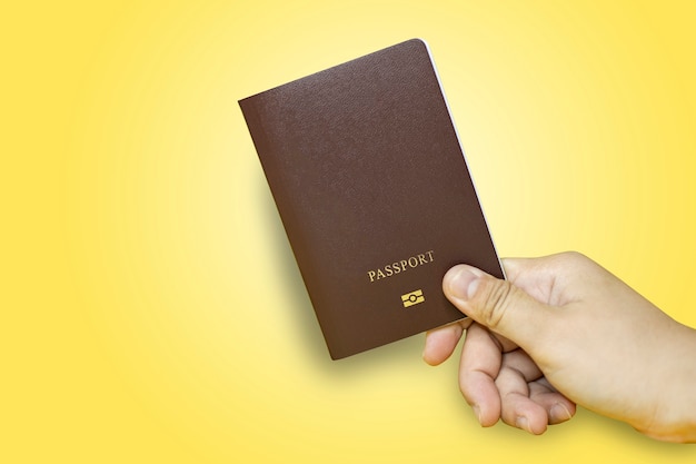 Bliska Dłoń Trzymająca Paszport W Kolorze Brązowym Z żółtym Tłem, Paszport Używany Do Podróży Międzynarodowych, Izolowany Na żółtym Tle. ścieżka Przycinająca Paszport.