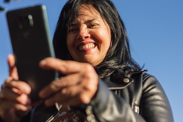 Bliska dorosła latynoska kaukaska kobieta na zewnątrz uśmiechnięta czytająca wiadomość tekstową przez telefon