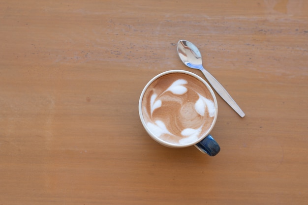 Bliska filiżankę gorącej kawy latte art na drewnianym stole.