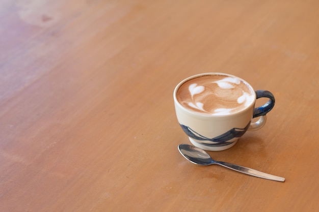 Bliska filiżankę gorącej kawy latte art na drewnianym stole.