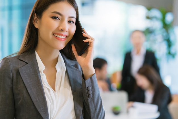 Bliska inteligentny atrakcyjny azjatycki biznes kobieta uśmiech ręka trzyma smartfon z nowoczesnym tłem biurowym
