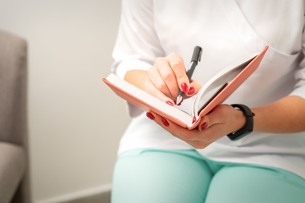 Bliska kobieta lekarz terapeuta pisze notatki w notatniku medycznym siedząc w gabinecie lekarskim