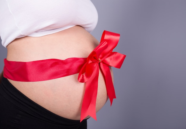 Zdjęcie bliska kobieta w ciąży z czerwoną wstążką prezent na brzuchu