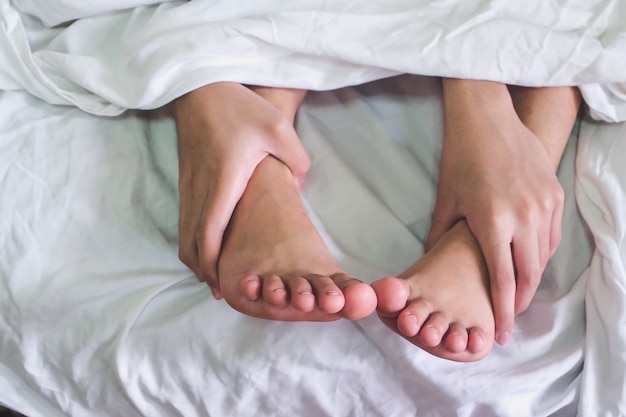 Bliska męskich i żeńskich stóp na łóżku i para seks w sypialni.