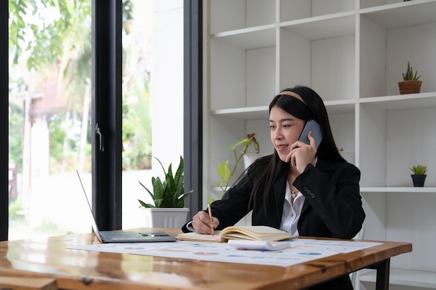 Zdjęcie bliska młoda kobieta azjatyckiego biura rozmawia z kimś na jej telefon komórkowy, patrząc w dal z szczęśliwym wyrazem twarzy