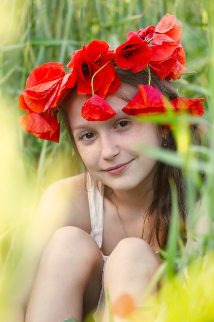 Bliska portret dziewczynki z diademem z maków siedzących na trawie