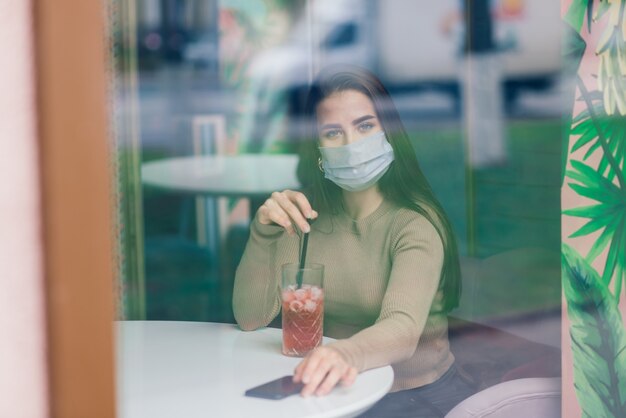 Bliska portret kaukaska kobieta ubrana w maskę medyczną i stojąca na ulicy przed kawiarnią