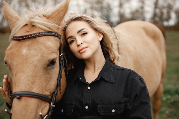 Bliska portret kobiety i konia. Blondynka i brązowy koń stojący w polu. Kobieta ubrana na czarno.