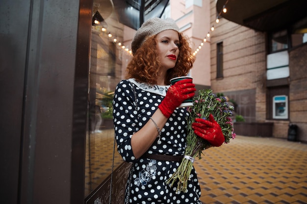 Bliska portret kobiety w sukni vintage trzymając filiżankę kawy na tle miasta