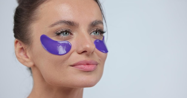 Bliska portret kobiety z fioletową przepaską na oko i dotykając jej twarzy, patrząc w kamerę Zabiegi kosmetyczne