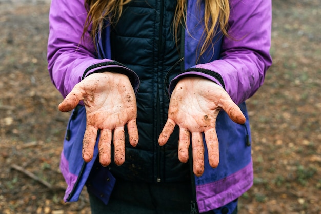 Zdjęcie bliska portret nierozpoznawalnej kobiety pokazującej jej dłonie pełne brudu podczas trekkingu w lesie