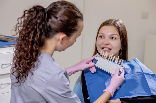 Bliska Portret Pięknej Młodej Damy Siedzi Na Fotelu Dentystycznym, Podczas Gdy Stomatologist Ręce W Sterylnych Rękawiczkach Trzymając Próbki Zębów.