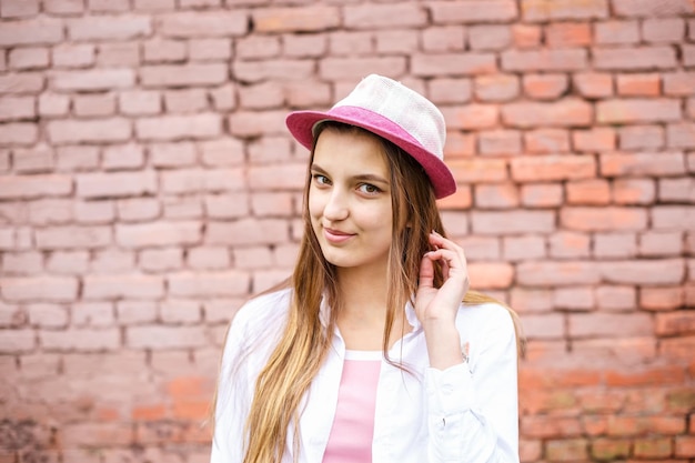 Bliska portret pięknej stylowej dziewczynki w kapeluszu w pobliżu różowego muru jako tła