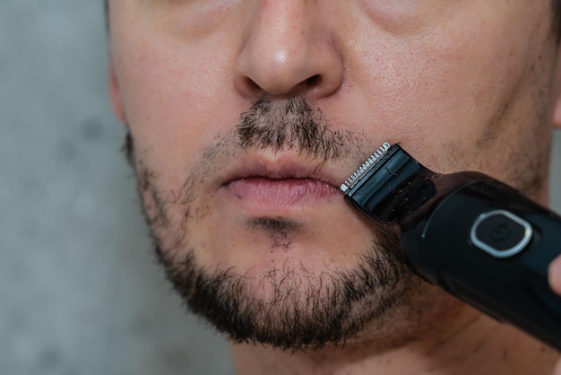 Zdjęcie bliska portret przystojnego mężczyzny golącego brodę elektrycznym trymerem poranna higiena