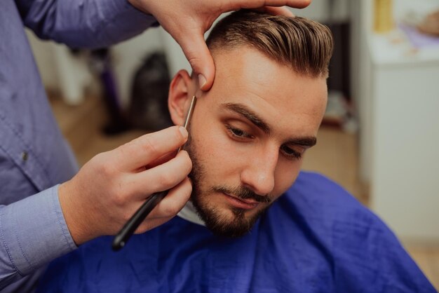 Bliska portret przystojnego młodego mężczyzny coraz golenie brody brzytwą Skupić się na ostrzu Selektywna ostrość Zdjęcie wysokiej jakości