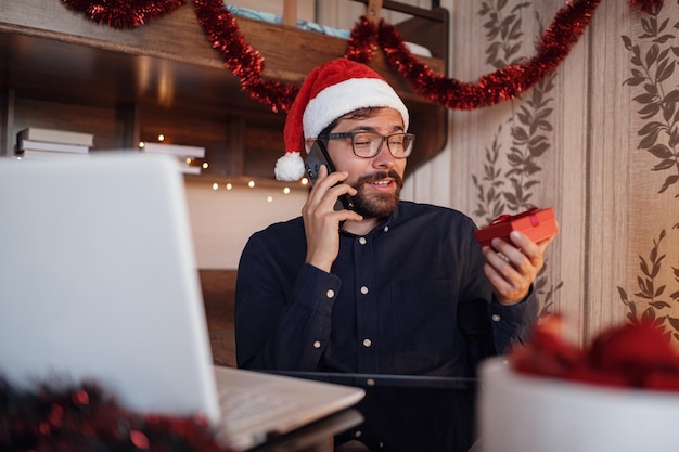 Bliska portret radosnego kaukaskiego przystojnego mężczyzny w santa hat siedzi w przytulnym pokoju