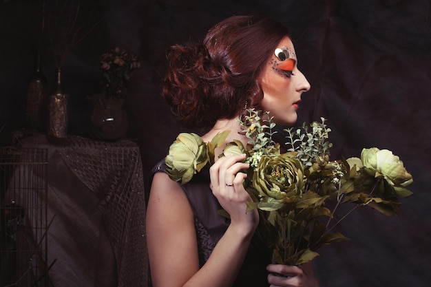 Bliska portret rudej kobiety z jasnym kreatywnym makijażem trzymającym suche kwiaty