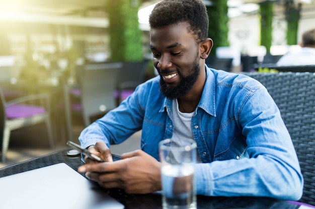 Zdjęcie bliska portret szczęśliwy afroamerykanin siedzący w kawiarni z telefonem komórkowym