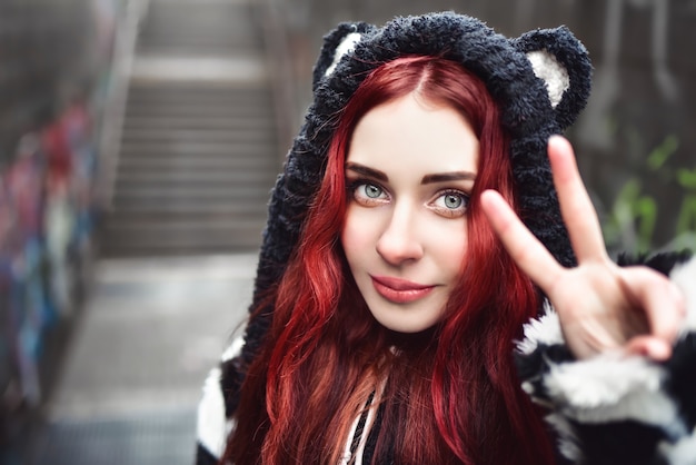 Bliska portret wesoły figlarny hipster nastolatka z rudymi włosami, który gestykuluje znak pokoju i uśmiech