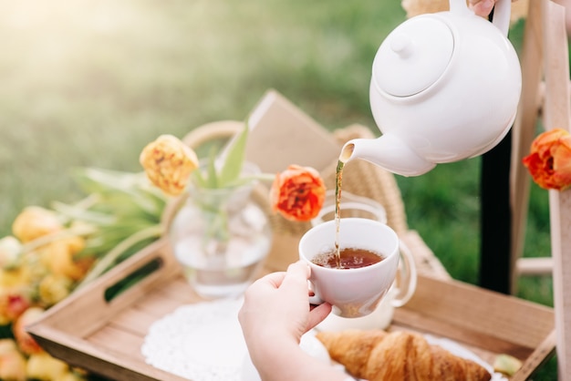 Bliska rąk wlewając herbatę w białej filiżance, wiosenny piknik ogrodowy