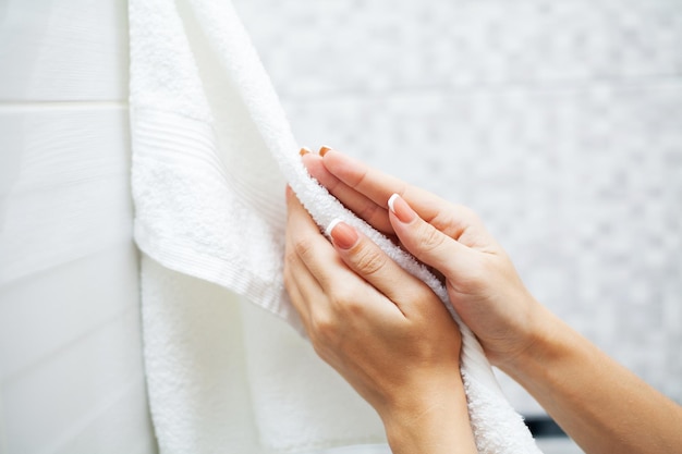 Bliska ręce używać białego ręcznika w jasnej łazience.