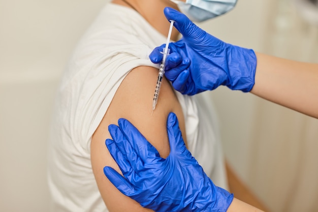 Bliska ręka lekarza szczepiącego przeciwko koronawirusowi Covid 19 młodemu mężczyźnie w gabinecie kliniki medycznej