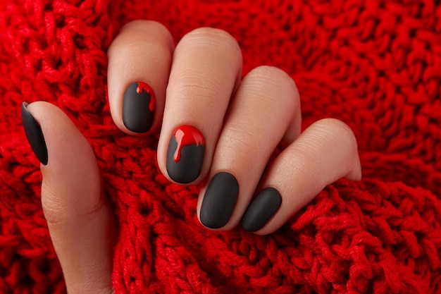 Bliska ręka womans z halloween manicure na czerwonym tle trzymając tkaninę Manicure pedicure koncepcja salonu piękności