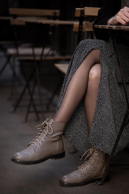 Bliska skrzyżowane nogi kobiety w skórzanych butach siedzącej w ulicznej kawiarni