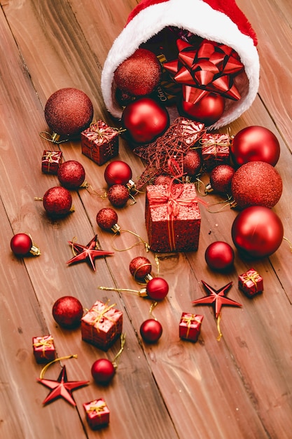 Bliska strzał czerwonych ozdobnych elementów wiszących gwiazda błyszczące kulki błyszczące kulki wstążka muszka i obecne pudełka wylewanie z Santa claus Boże Narodzenie kapelusz na ciemnobrązowy drewniany stół z miejsca kopiowania.