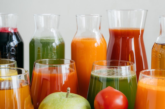Bliska strzał szklanych butelek wypełnionych kolorowym sokiem z różnych warzyw i owoców czerwony pomidor i zielone jabłko na pierwszym planie Świeży napój detox