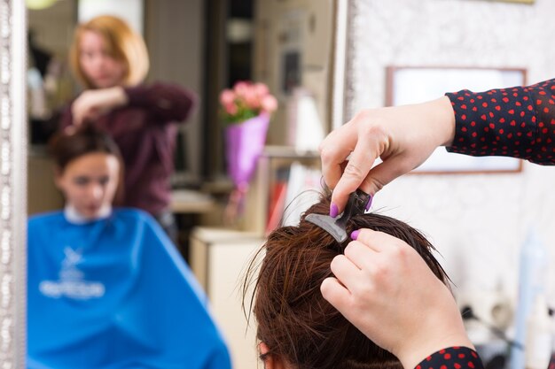 Bliska stylista wkładanie klipsa do mokrych włosów klientki brunetka w salonie z niewyraźne odbicie w tle lustro