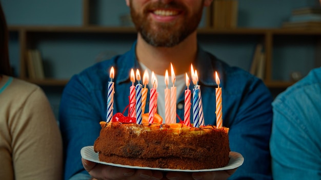 Bliska uroczysty tort z płonącymi świeczkami szczęśliwy brodaty nierozpoznawalny urodzinowy mężczyzna uśmiecha się